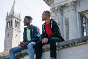 Two students sit in front of Bancroft Library with the Campanile in the background.
