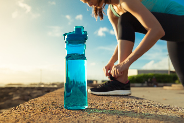 A runner ties their shoes while their water bottle sits in the foreground.